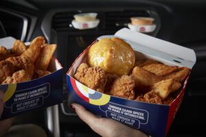 Two Krispy Krunchy Chicken combo boxes with fried chicken, potato wedges, and honey biscuits being held inside a car.