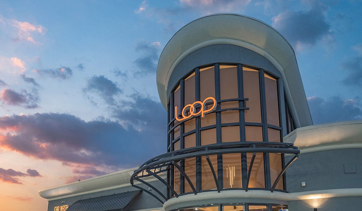 Modern Loop convenience store exterior at sunset with curved architectural design, illuminated signage, and large glass windows.
