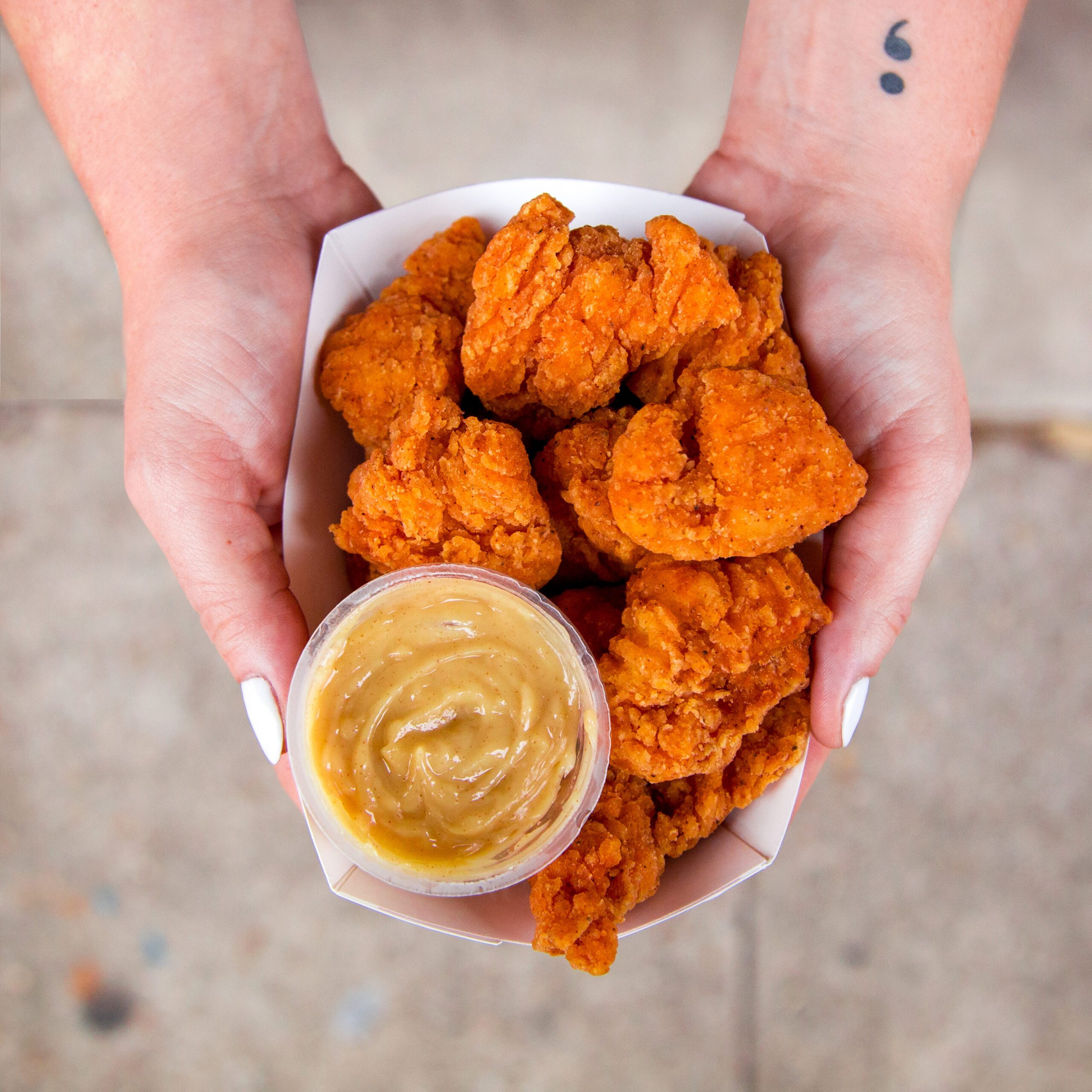 Hands holding a box of Krispy Krunchy Chicken® boneless wings served with a cup of creamy signature dipping sauce.