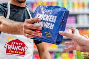 Krispy Krunchy Chicken team member hands a packaged Cajun Chicken Sandwich to a customer in a convenience store