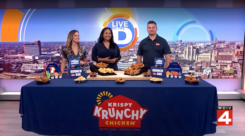 Krispy Krunchy Chicken team member joins WDIV Local 4 hosts in studio with a table full of fried chicken, sides, sauces, and Krunch Box meals.