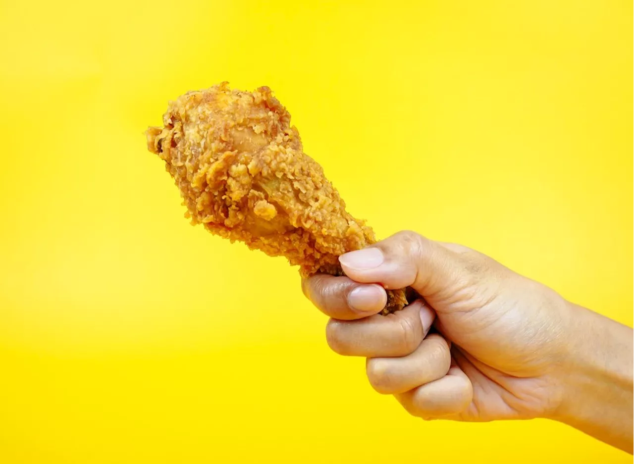 Hand holding a crispy fried chicken drumstick against a bright yellow background